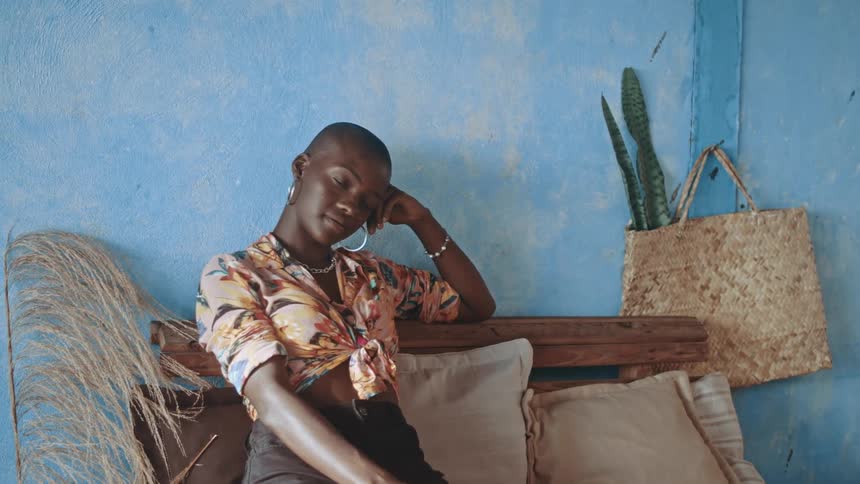 A stylish person poses thoughtfully on a cozy indoor bench