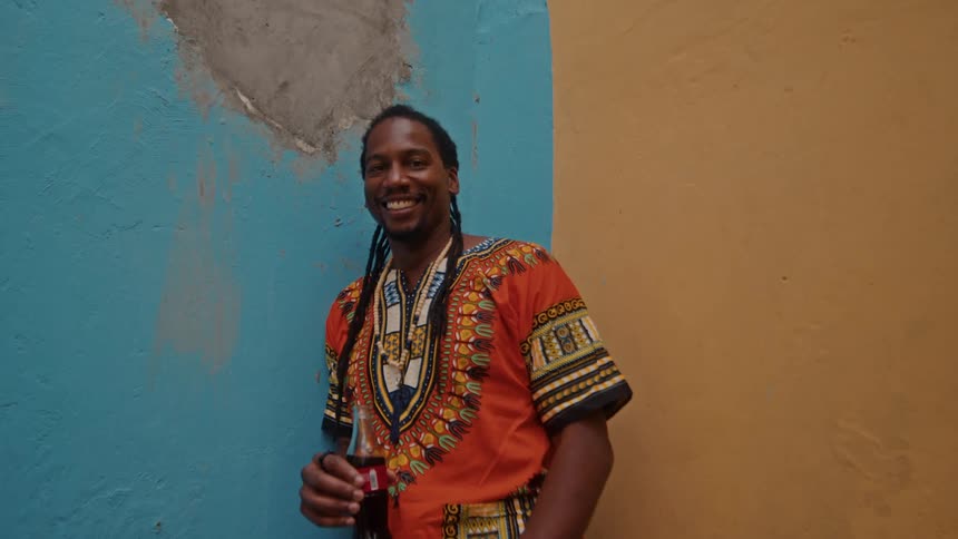 A smiling man poses with a soda against a colorful wall