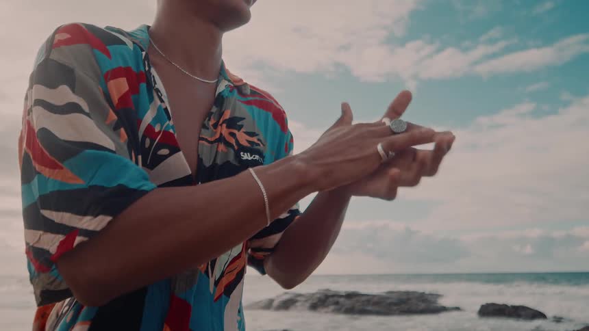 A man is on a beach wearing a flowery shirt and he is clapping happily