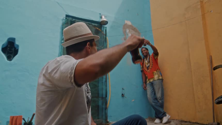 Two men raise their drinks in a colorful courtyard enjoying a relaxed moment together