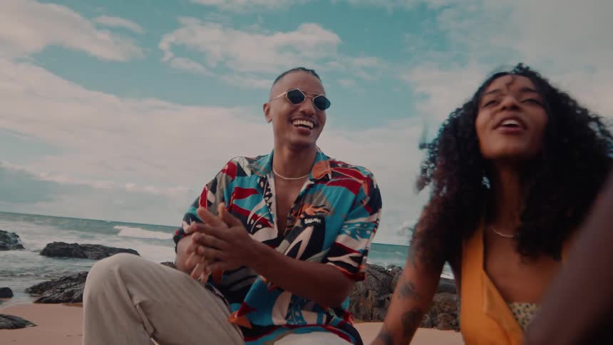 A man and woman sit on rocks at the beach smiling and chatting playfully