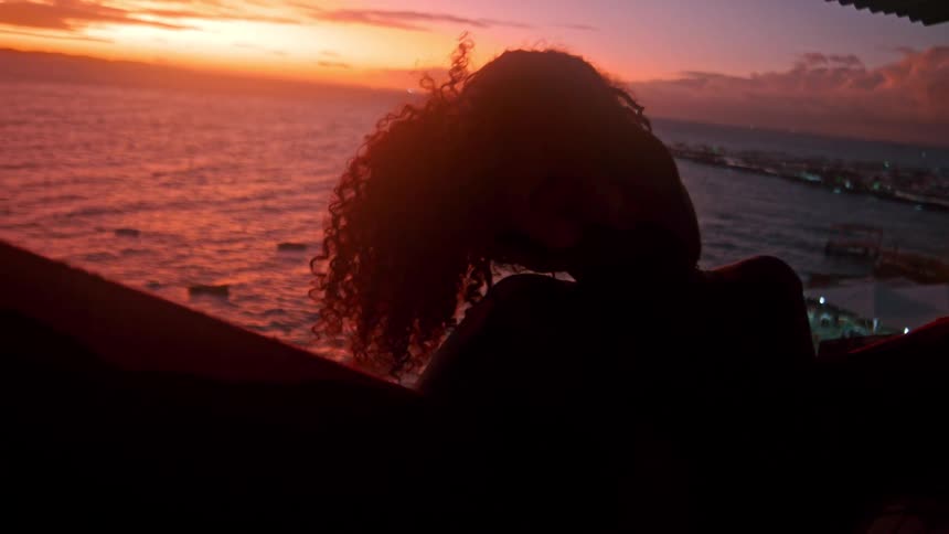 Silhouette of a curly haired woman relaxing on the seaside balcony with reddish sky
