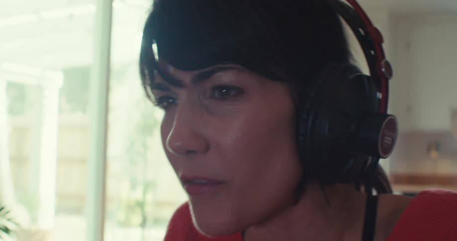 A woman with short dark hair and headphones is focused on a screen at home