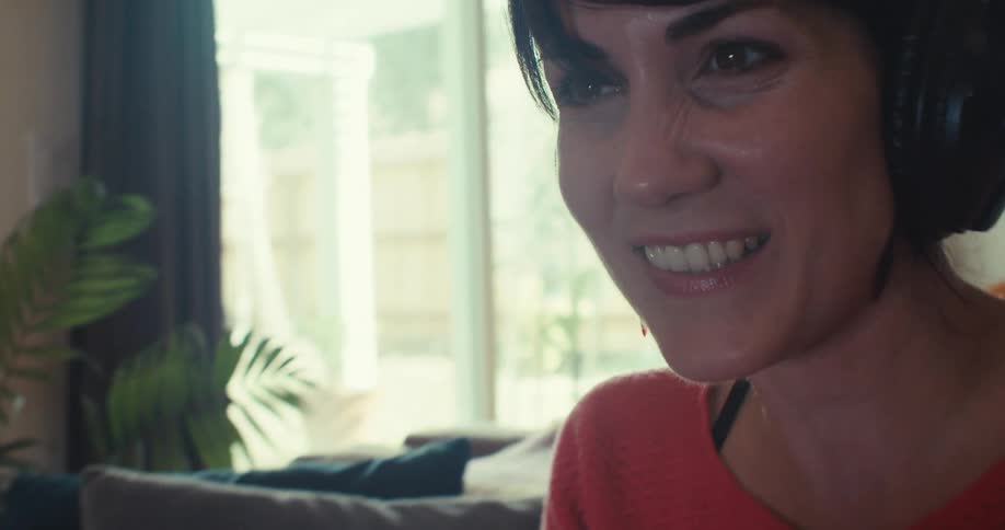 Close up of a woman smiling while gaming with a game controller and headset in a living room during daytime