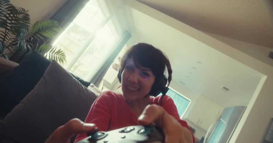 A young woman sitting on her couch at midday wearing a headset and enjoying a fun gaming session