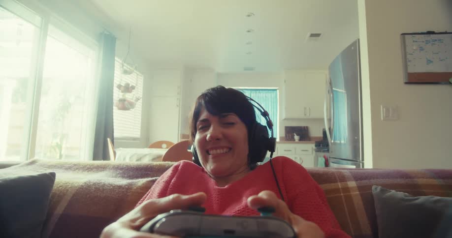 Young woman plays video games with a controller while sitting in a living room and celebrates after winning