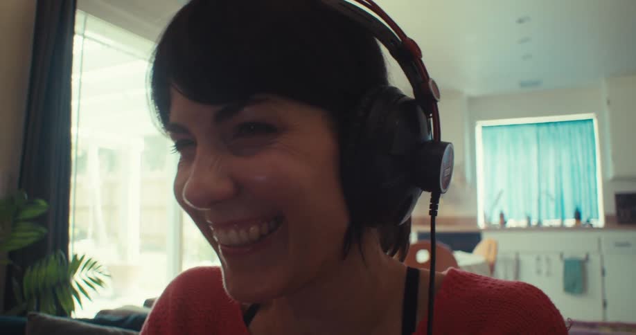 Close up of a young woman smiling and gaming with a controller and headset while sitting in a living room during daytime