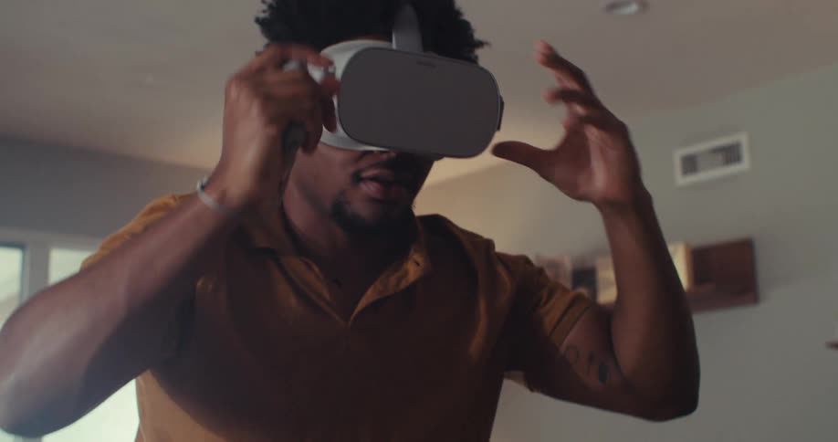 Close up of a young black man experiencing virtual reality goggles while standing in a living room during daytime