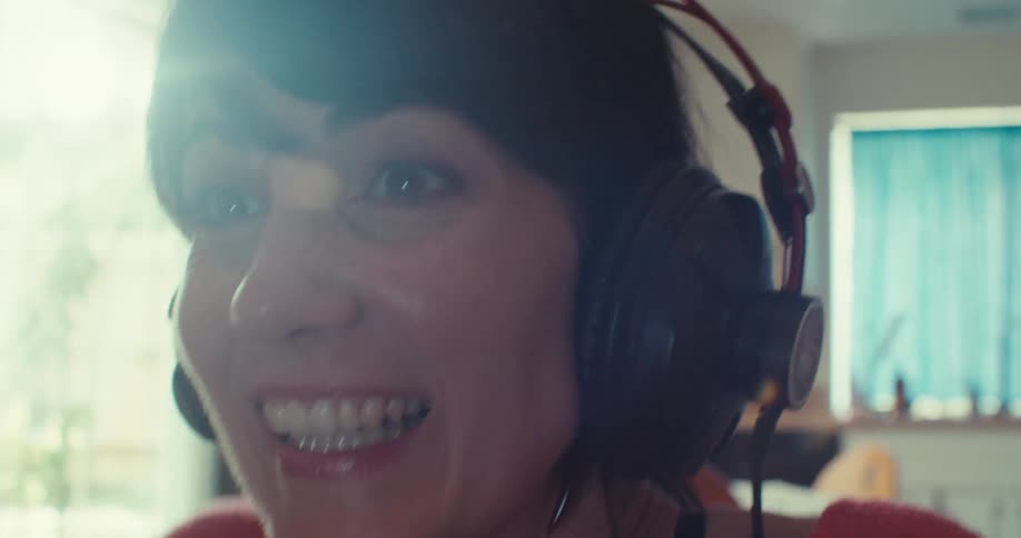 A woman is laughing and talking while wearing headphones