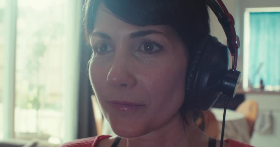 A female gamer wearing headphones sits on a couch indoors fully immersed and enjoying her gaming session