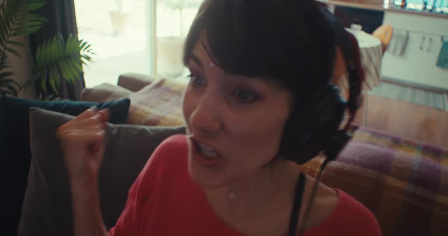 A female gamer wearing a headset looks excited during a gaming session while sitting on a couch at midday