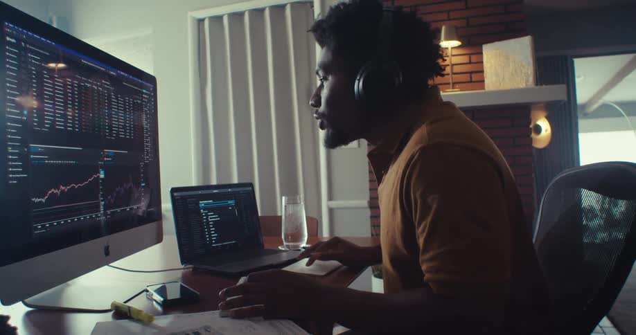 Man in headphones works at a multiscreen desk in home office