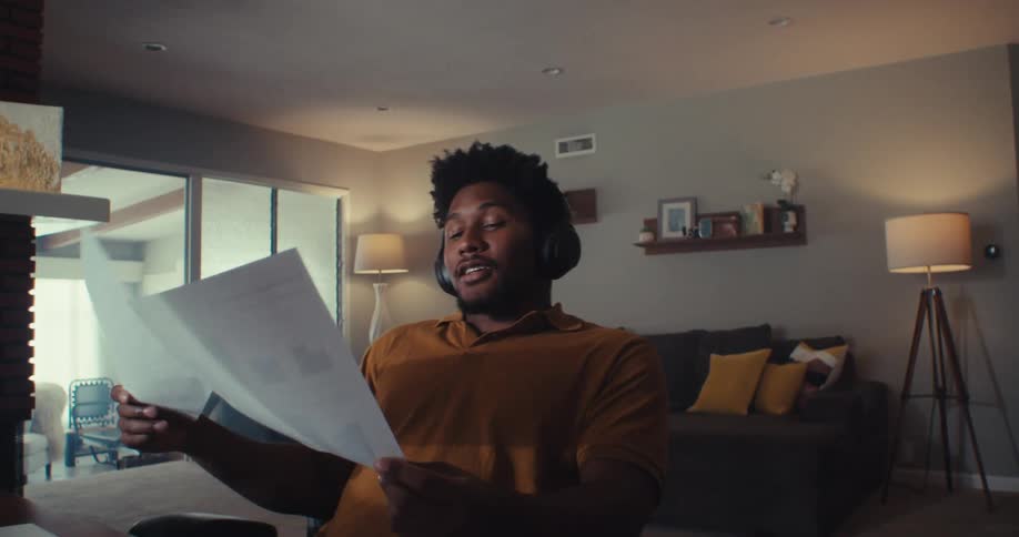 A man wearing headphones chats during a video call at his home workspace