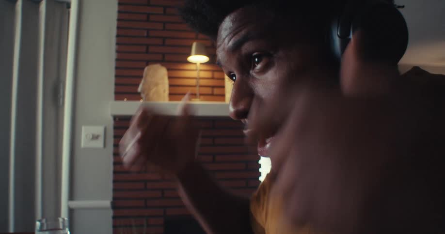 A young black man wears headphones while on a video call seated in front of a computer