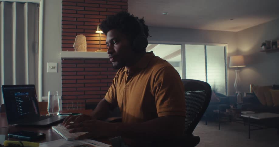 Man works on a computer at home with papers and a monitor in front of him