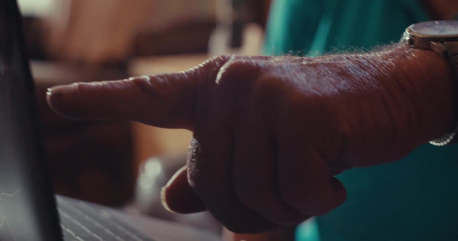 Close up of an elderly mans hand pointing to a laptop screen while sitting in a living room