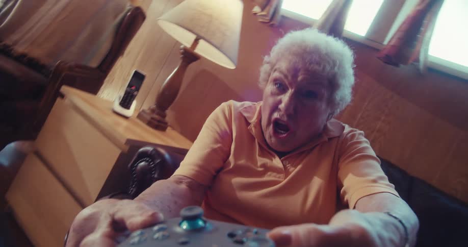 An elderly woman intensely plays a video game with a controller while sitting on a couch