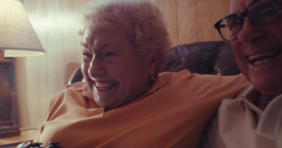 An elderly couple laughs joyfully while sitting close together on a couch