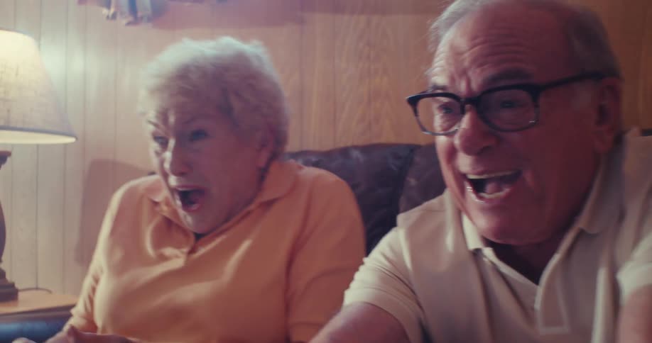 An elderly couple excitedly plays a video game together on a couch