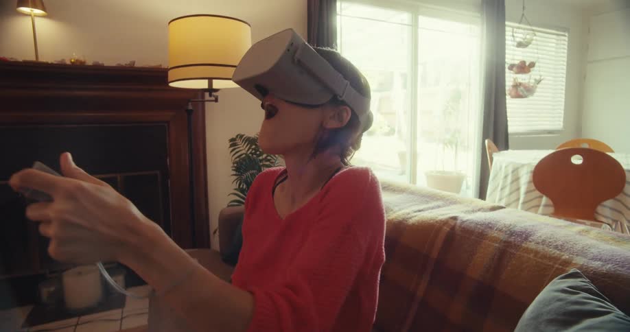 Young woman turns from side to side while sitting in a living room as she plays a virtual game with vr goggles
