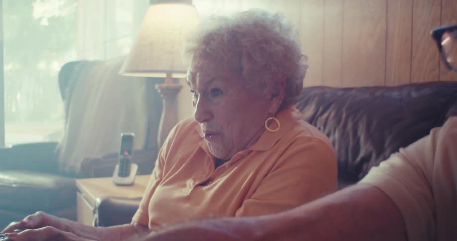 An elderly couple sitting on a sofa and the man is laughing and both are looking straight ahead