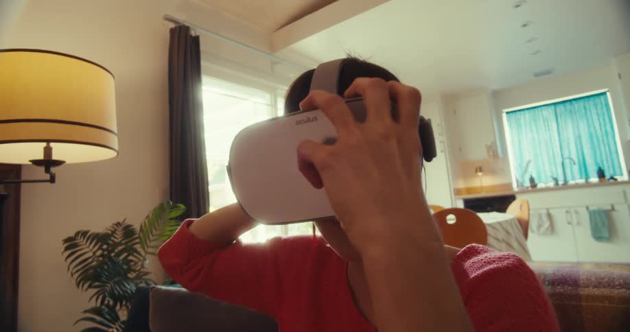 Close up of a young woman putting on vr googles while sitting on a couch in the living room