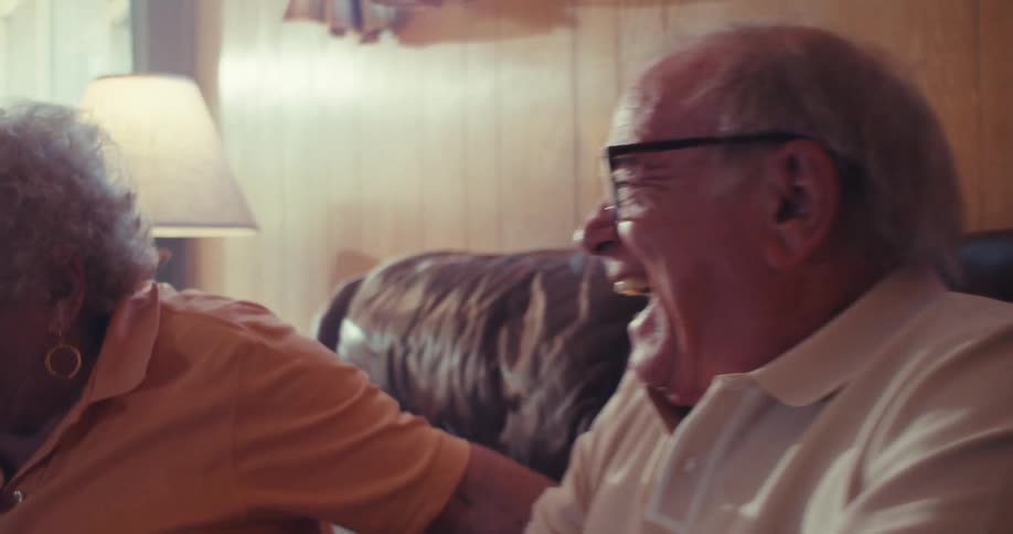 An elderly man and woman happily playing video games together on a couch