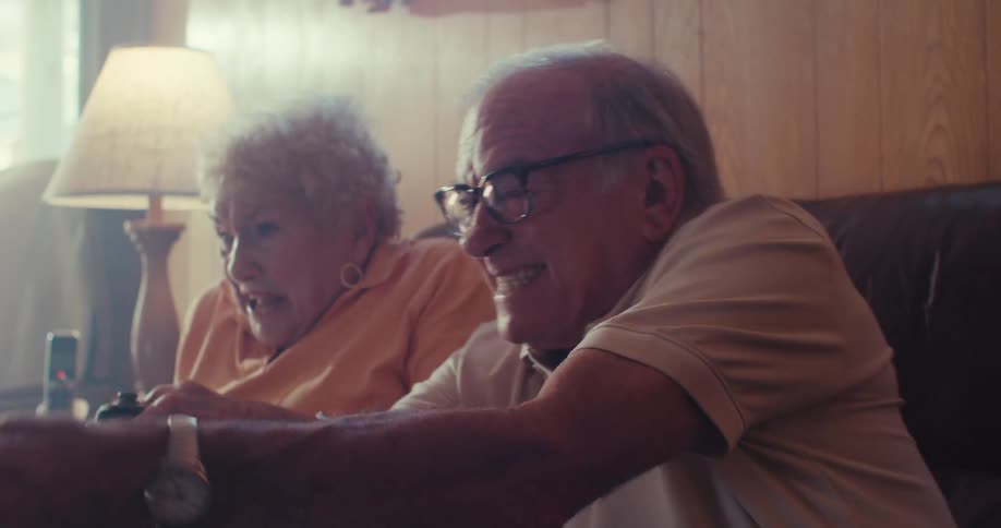 Two elderly people excitedly play a video game together on a couch