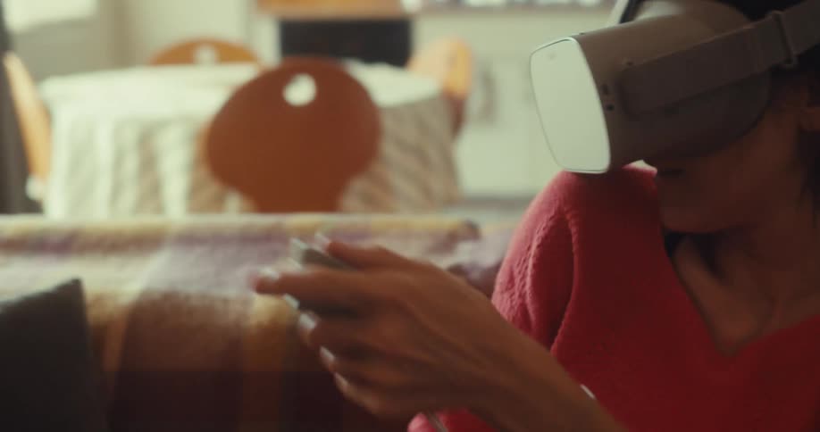 The woman waves the controller around while using a virtual reality headset on the couch