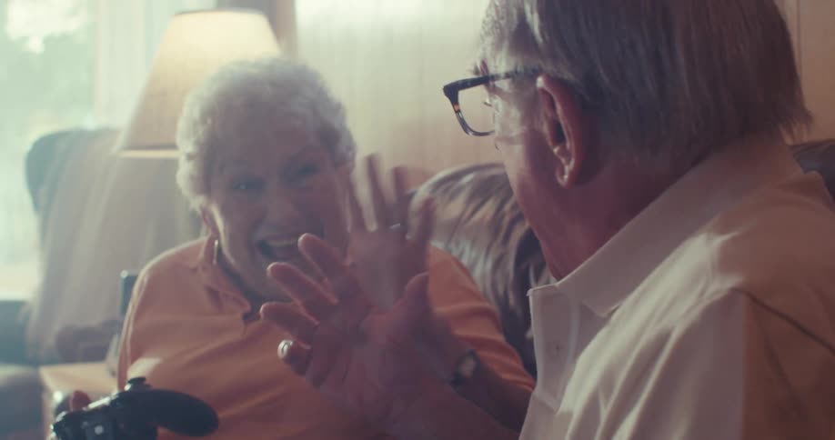 Elderly couple excitedly play video games together on a couch