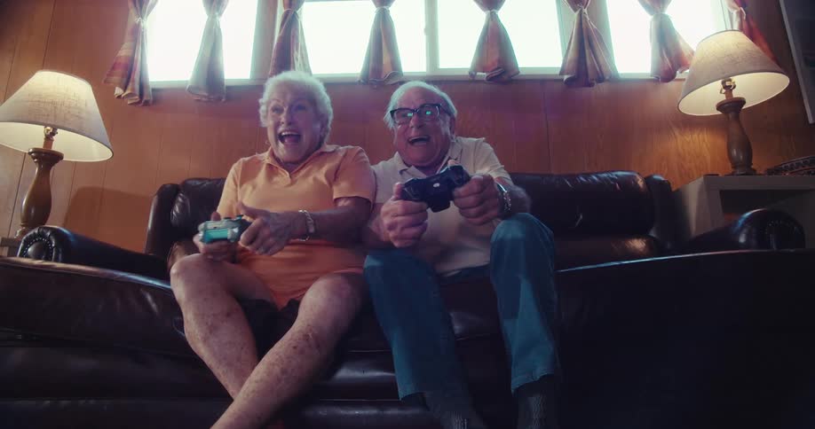 Elderly couple laughing while playing video games on a couch