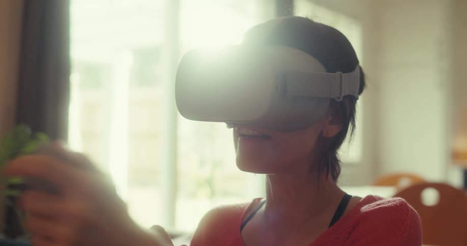 A woman wearing a virtual reality headset and holding a controller is seated in a cozy sunlit room
