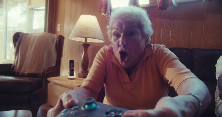 Elderly woman screams as she plays video games with a controller while seating in a living room during daytime