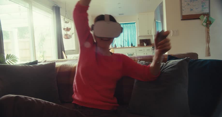 A young woman sits on a couch wearing a vr headset having a fun time around midday