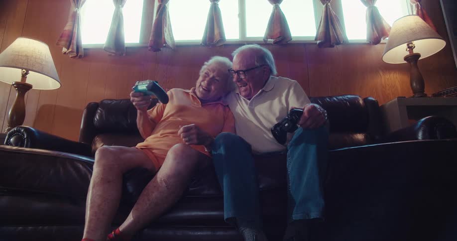 Elderly couple sitting on a leather sofa holding video game controller and having a great time