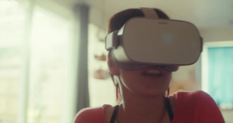 A woman wearing a vr headset sits on a couch having a fun time around midday in her living room