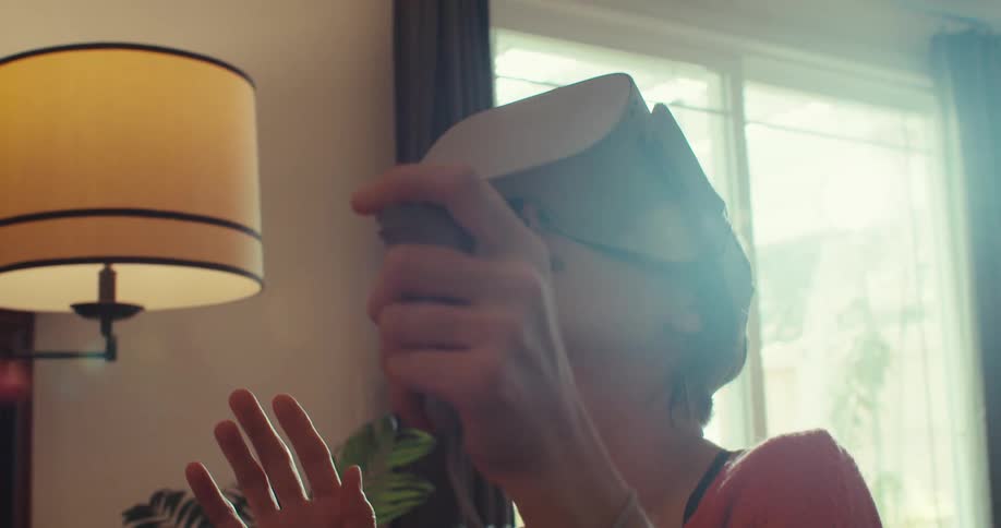 A woman uses a vr headset and controller in a brightly lit living room