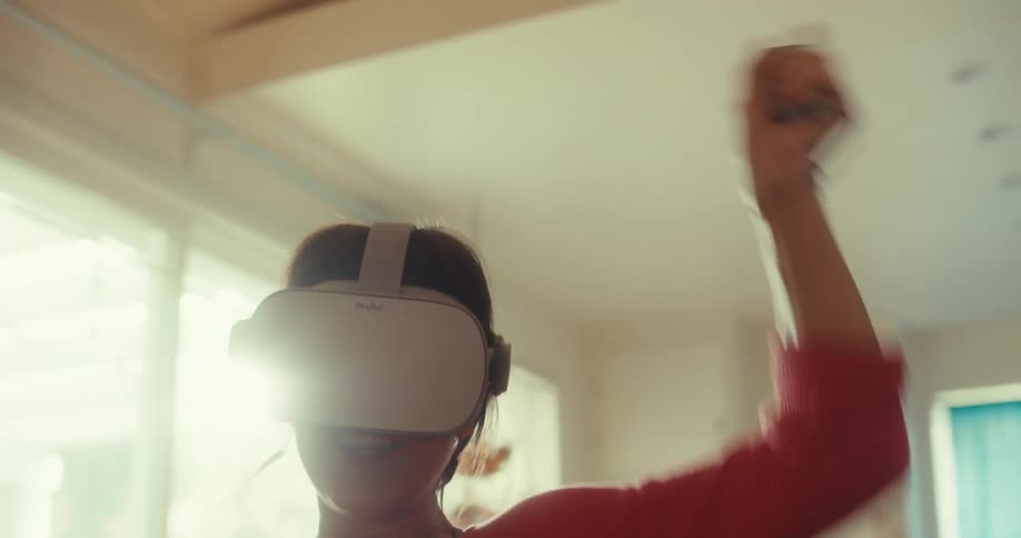 Close up of a young woman playing and celebrating a virtual reality game with vr goggles while sitting on a couch in the living room during daytime