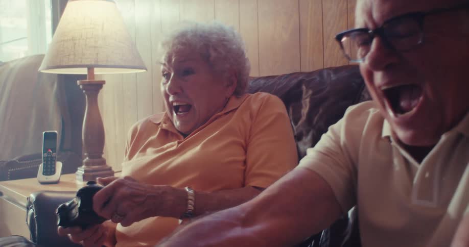 An elderly couple enjoying a fun time gaming in their living room sitting on the couch around midday