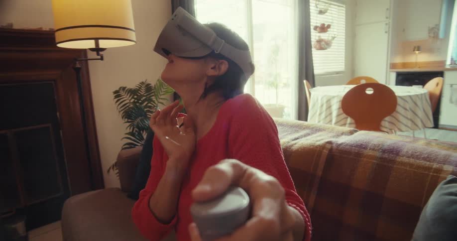A young woman wearing a vr headset sits on a couch enjoying a fun and immersive experience