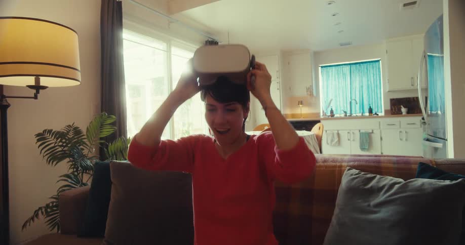 The woman raises her arms and removes the virtual reality headset