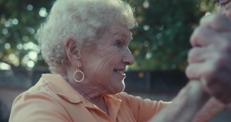 Elderly couple joyfully dances hand in hand in backyard