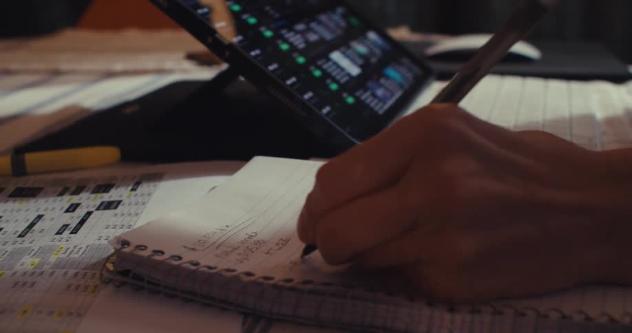 Left handed person writing notes on spiral notebook