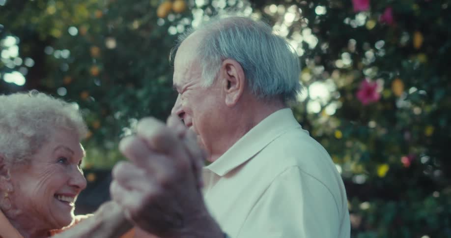 An elderly couple dances together joyfully in a garden