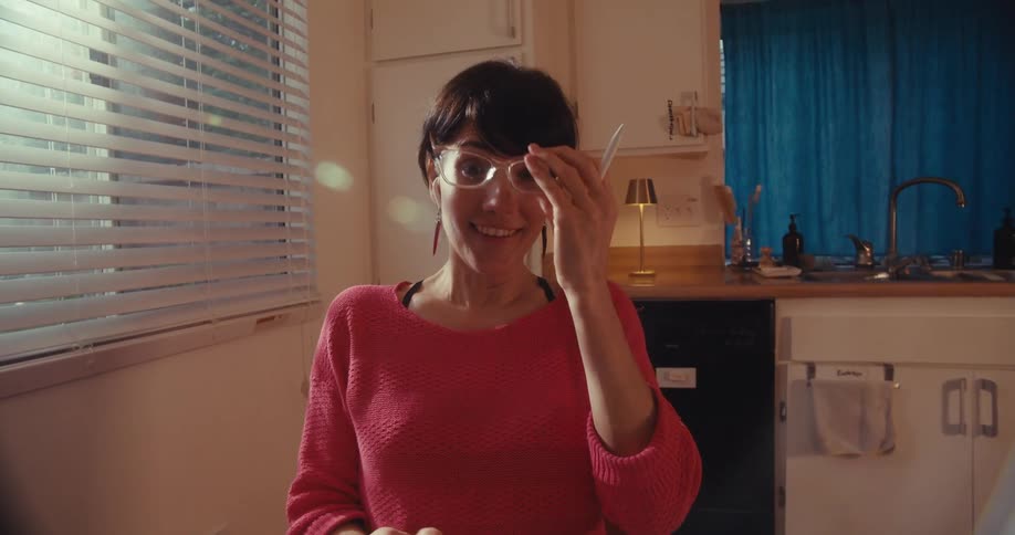 A woman working on a tablet at her kitchen table has a happy realization and begins to gesture excitedly during a video call