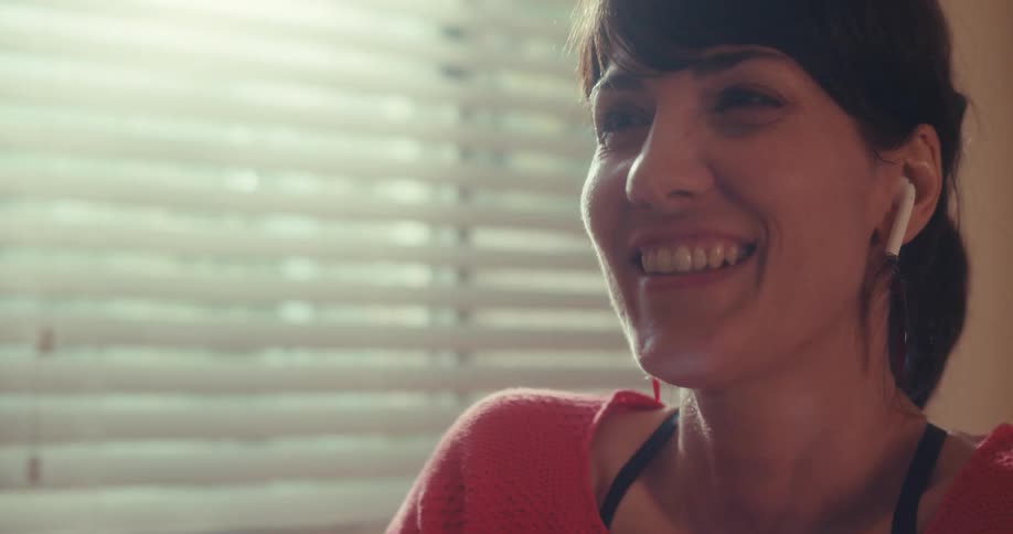 A woman wearing glasses sits by a sunlit window speaking to someone off camera