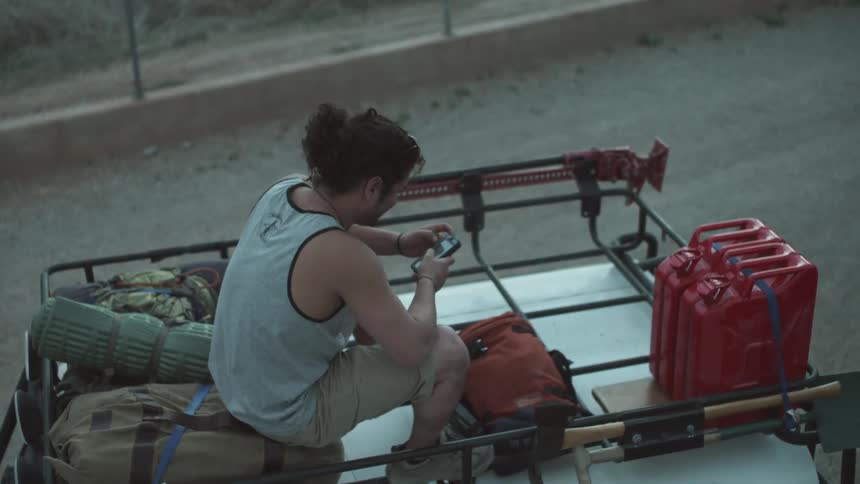 Man sits on a car roof with smartphone