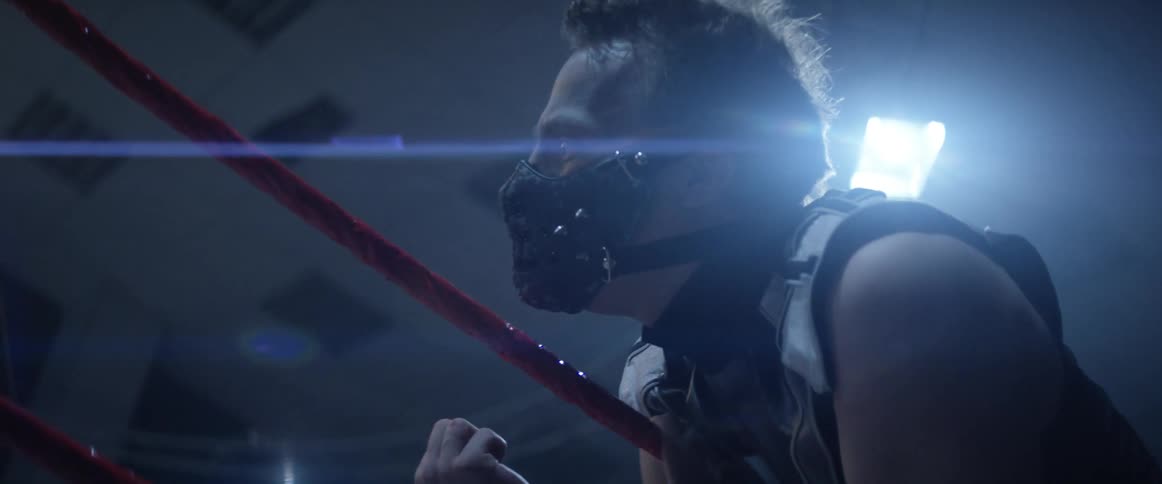 A wrestler with a mask leans on the rope