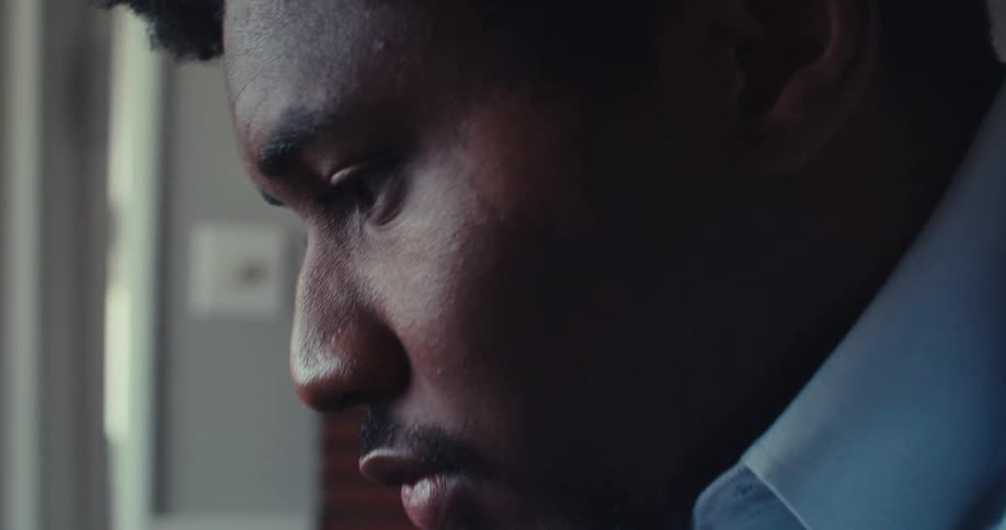 A young black man sits in his office behind a desk typing on his laptop with a glass of water beside him
