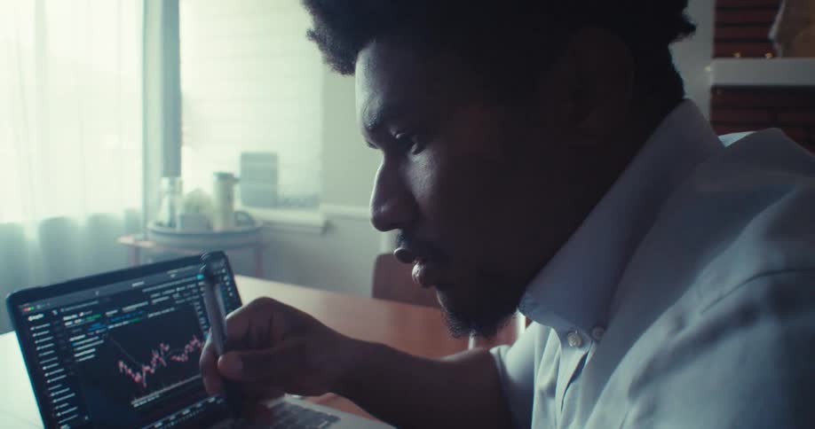 Man studies financial data and checks stock charts on laptop